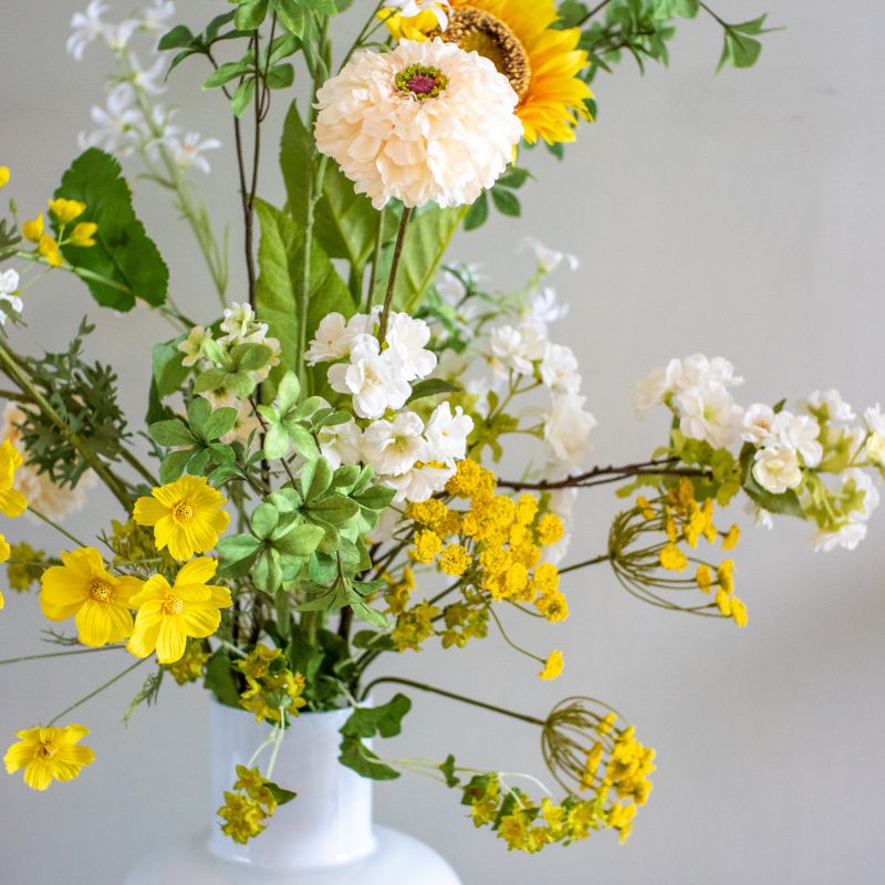 close up van kunstboeket aaf bestaande uit gele Zonnebloemen, witte dahlia's,
gele Gypsohilia's en witte jasmijntjes. zijden bloemen zijn te bestellen bij bloomfever